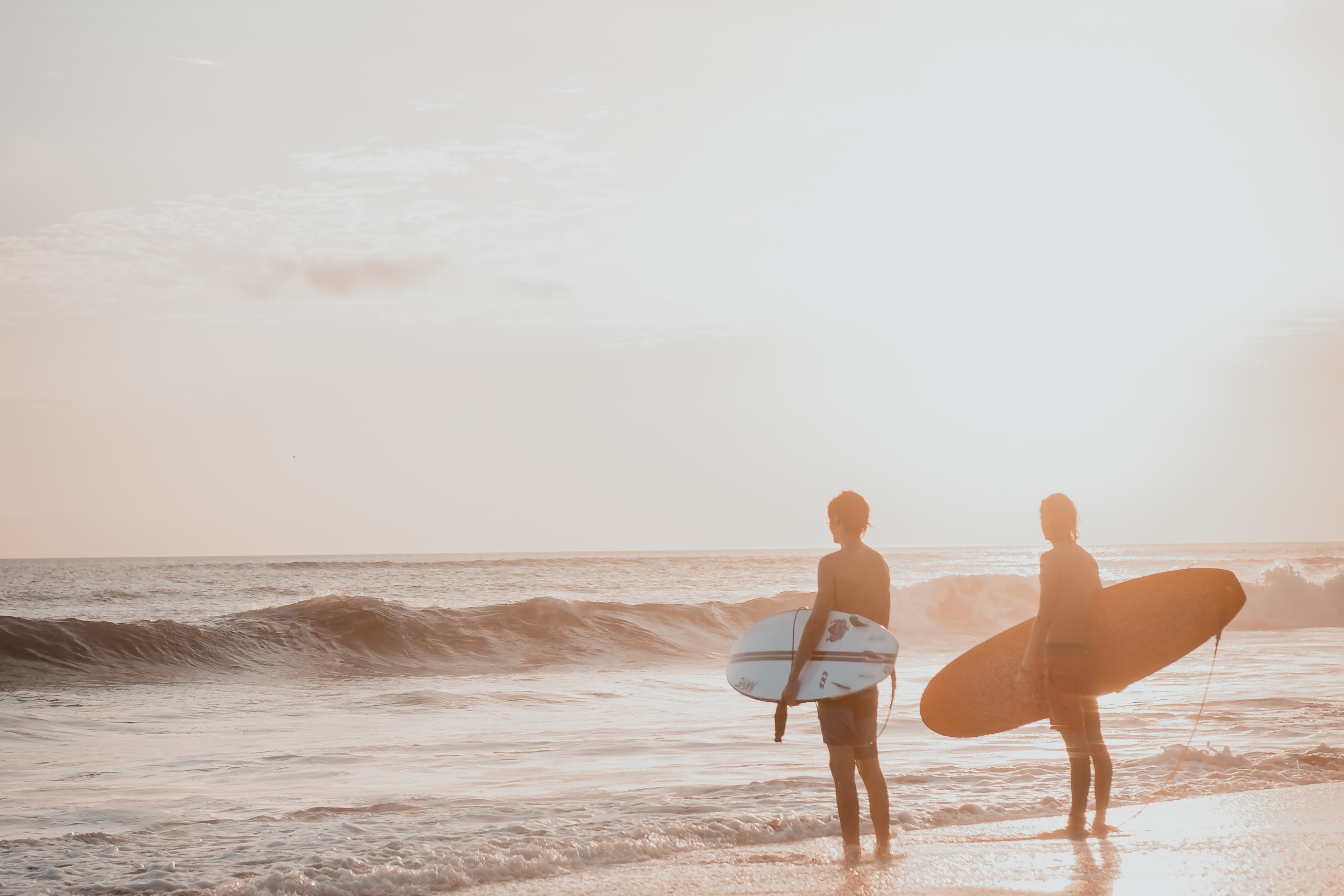 two surfers on their way to their sunset surf facing the wave